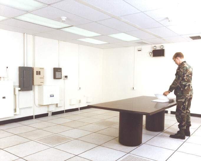 Man i uniform står vid bord i avlyssningssäkert rum